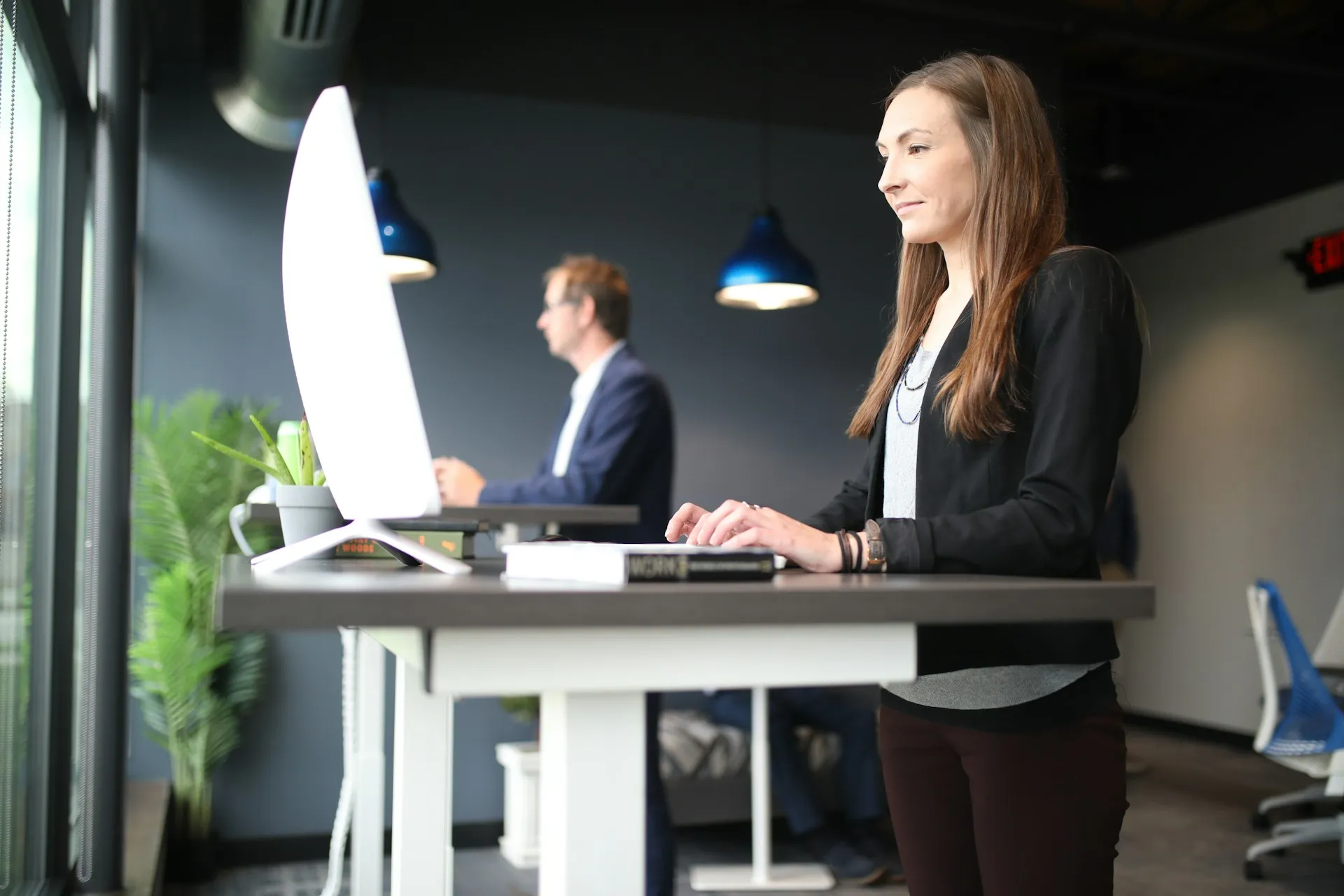 Woman standing at an adjustable standing desk with elbows bent at a natural angle and shoulders relaxed while typing